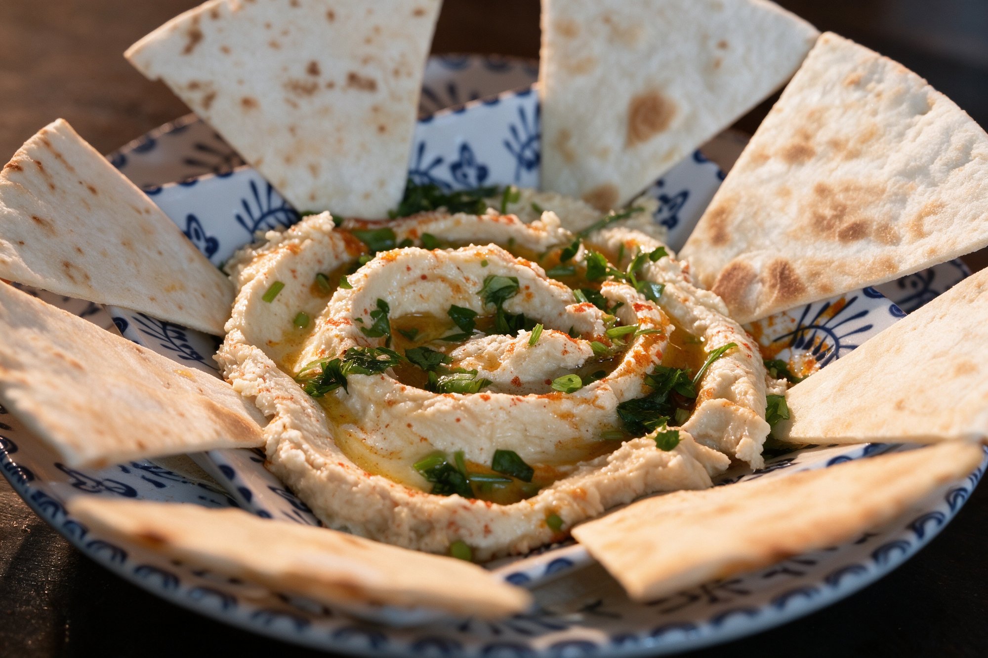 Hummus con aceite de oliva, pimentón, perejil y pan pita tostado en triángulos
